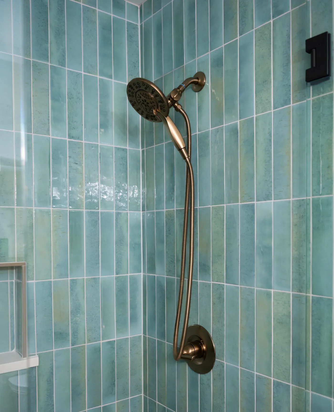 Brushed brass shower head against green vertical tile