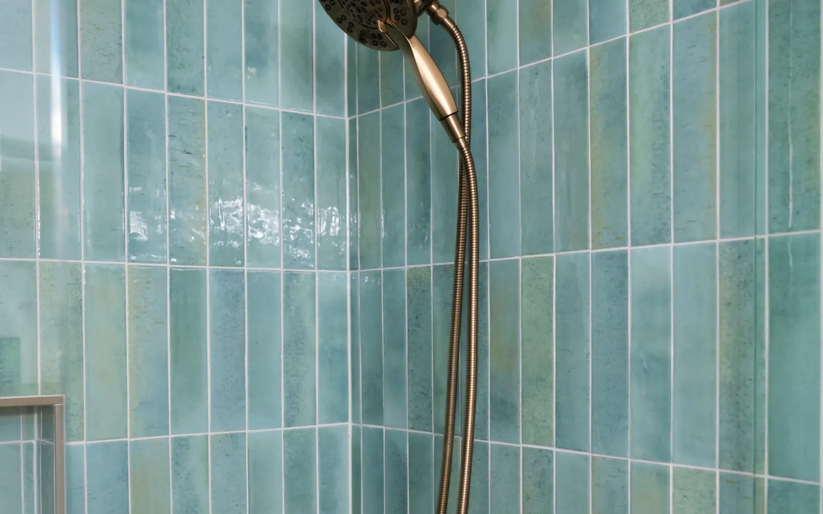 Brushed brass shower head against green vertical tile