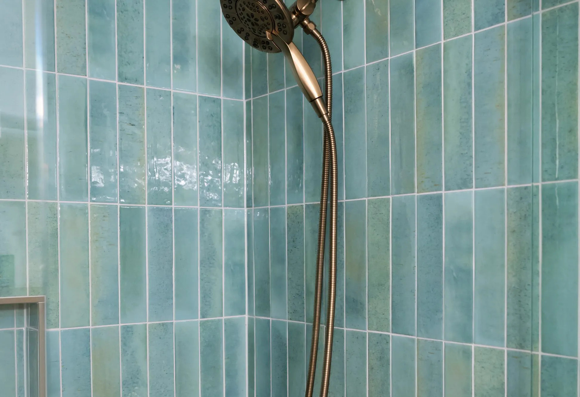 Brushed brass shower head against green vertical tile