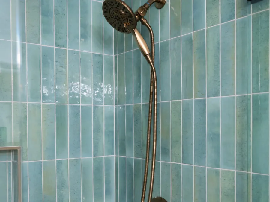 Brushed brass shower head against green vertical tile