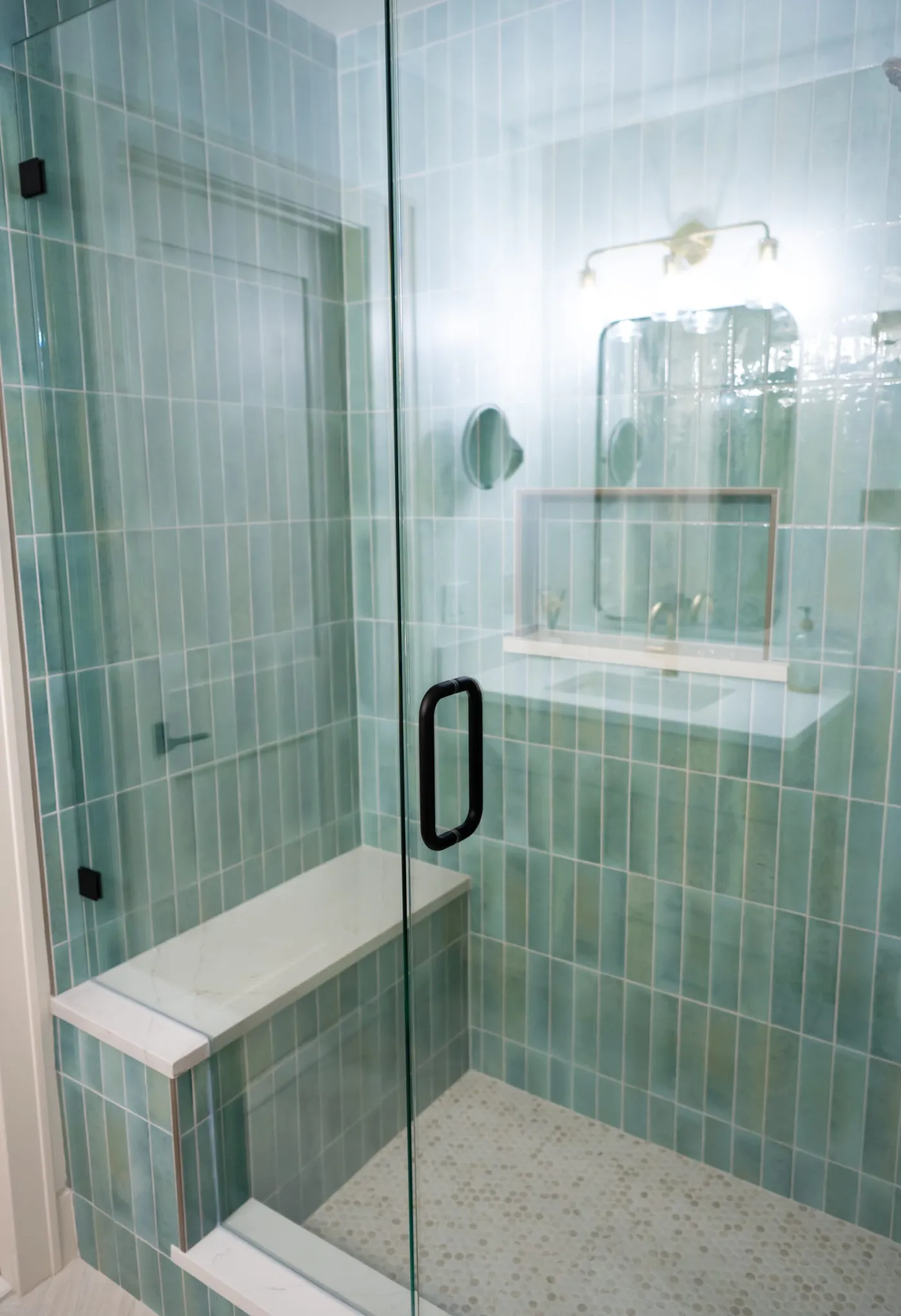 Frameless glass shower door with a quartz bench and green tile surround